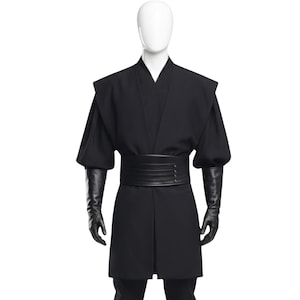 Puede incluir: Un disfraz negro exhibido en un maniquí. El disfraz incluye una túnica larga, un cinturón ancho y guantes largos. La túnica tiene cuello en V y mangas cortas. El cinturón está hecho de múltiples bandas horizontales. Los guantes son largos y ajustados.