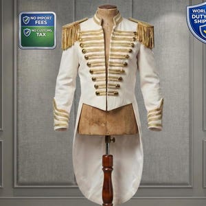 Puede incluir: Una chaqueta blanca de estilo militar con adornos dorados, botones y charreteras. La chaqueta tiene un cuello alto y una cola larga y dividida. Las mangas tienen detalles dorados en los puños. La chaqueta se exhibe en un maniquí.