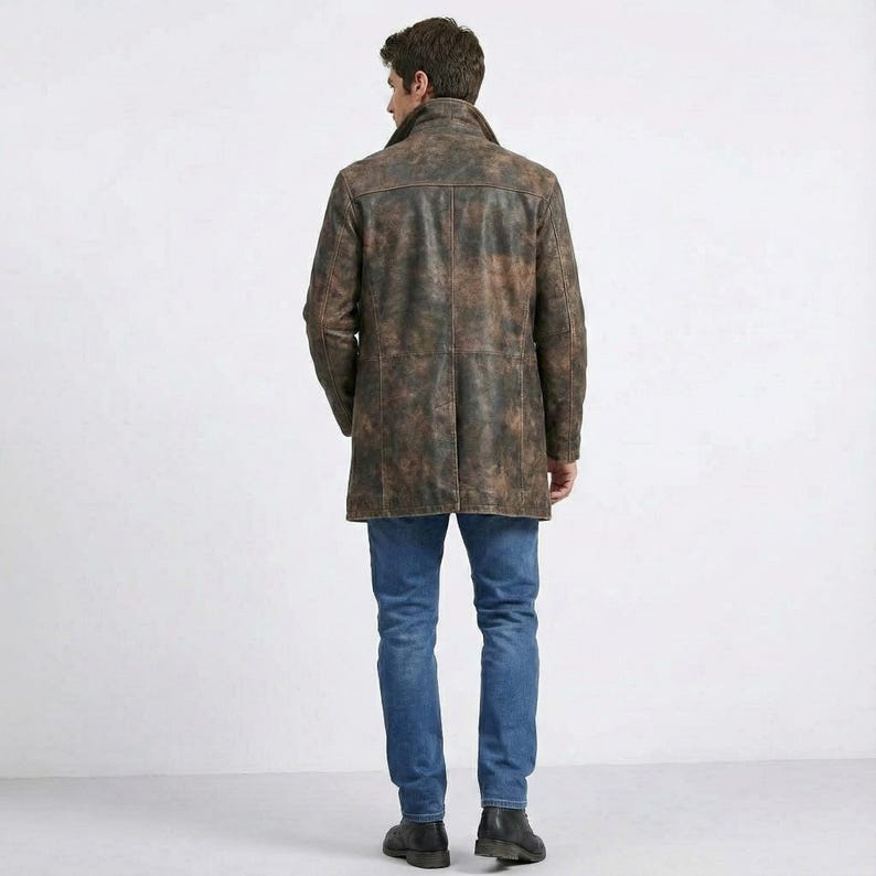 May include: A brown leather coat with a distressed finish. The coat has a classic design with a collar and a button-down front. The person is wearing blue jeans and black boots.