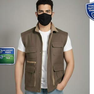 Puede incluir: Un chaleco marrón con múltiples bolsillos y un cuello beige. El chaleco se usa sobre una camiseta blanca. La imagen también muestra una mascarilla negra. El chaleco tiene cierre de cremallera y está hecho de un material duradero.