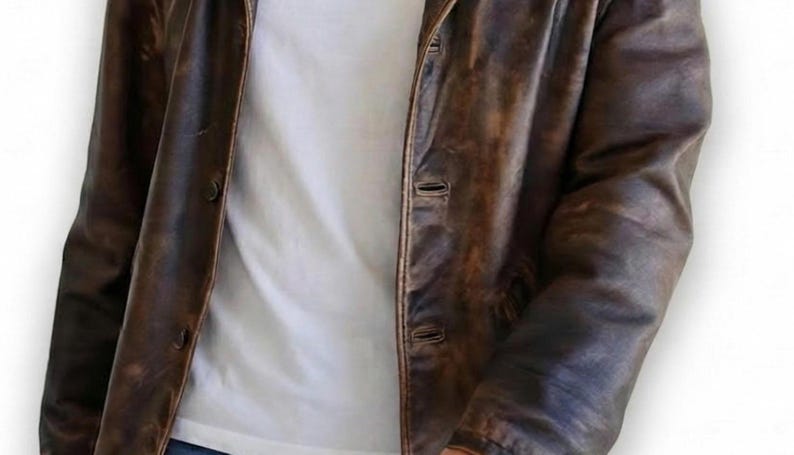 May include: A brown leather jacket with a distressed finish. The jacket has a button-up front and a classic collar. The jacket is worn over a white t-shirt. The leather appears to be worn and textured.