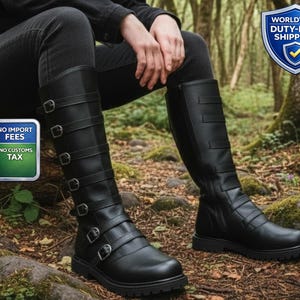 May include: Black knee-high boots with multiple buckle straps. The boots have a side zip and a thick, lug sole. The image is set in a forest setting.