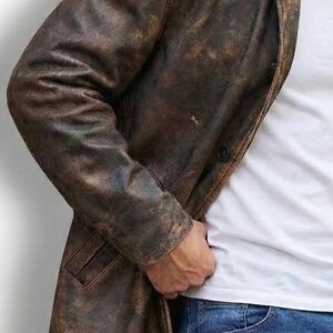 May include: A distressed brown leather jacket with a classic lapel collar and a single-button closure. The jacket has a worn, textured appearance, suggesting a vintage or rugged style. The model is wearing a white t-shirt and blue jeans.