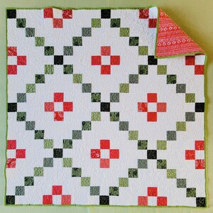 May include: A handmade quilt with a white background and a repeating pattern of red, green, and black squares arranged in diagonal lines. The quilt features red cross-shaped designs and a green border. The reverse side has a red floral pattern.