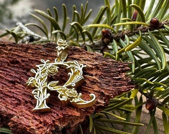 Peut inclure: Un pendentif en forme de lettre "R" de couleur dorée avec des motifs floraux complexes et des roses.