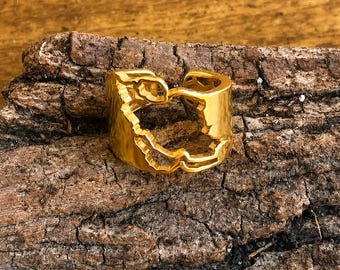 Peut inclure: Une bague ouverte de couleur dorée présentant un design découpé qui ressemble à la forme d'une carte. L'anneau a une finition lisse et polie avec un bord irrégulier et organique qui suit les contours de la découpe, créant un centre creux.
