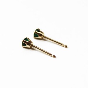 May include: A pair of gold stud earrings with small green emerald stones.