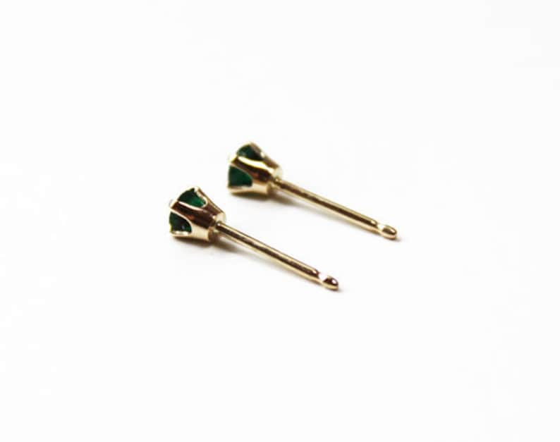 May include: A pair of gold stud earrings with small green emerald stones.