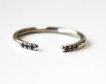 Op de afbeelding: Een zilveren ring met een opening aan één kant, versierd met een rij kleine zwarte diamanten.