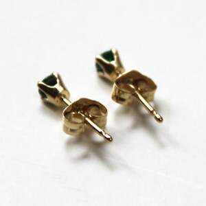 May include: A pair of gold stud earrings with small green gemstones.
