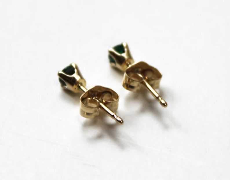 May include: A pair of gold stud earrings with small green gemstones.