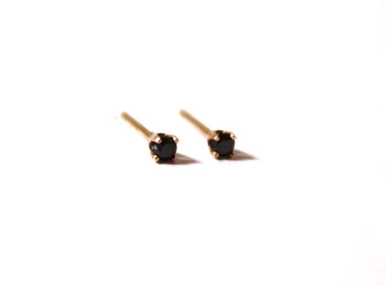 K&ouml;nnte beinhalten: Ein Paar goldene Ohrstecker mit kleinen schwarzen Edelsteinen.