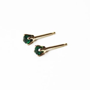 May include: A pair of gold stud earrings with small, round, emerald green gemstones.