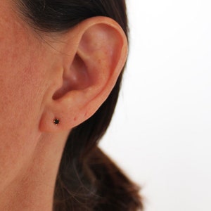 K&ouml;nnte beinhalten: Nahaufnahme eines Ohrs mit einem kleinen schwarzen Ohrstecker.