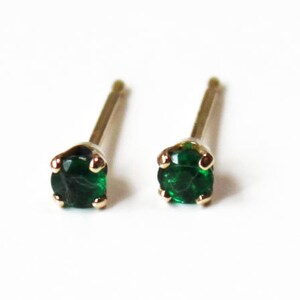 May include: A pair of small, gold stud earrings with green gemstones. The earrings are simple and elegant.