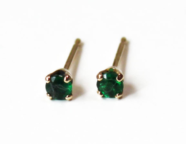 May include: A pair of small, gold stud earrings with green gemstones. The earrings are simple and elegant.