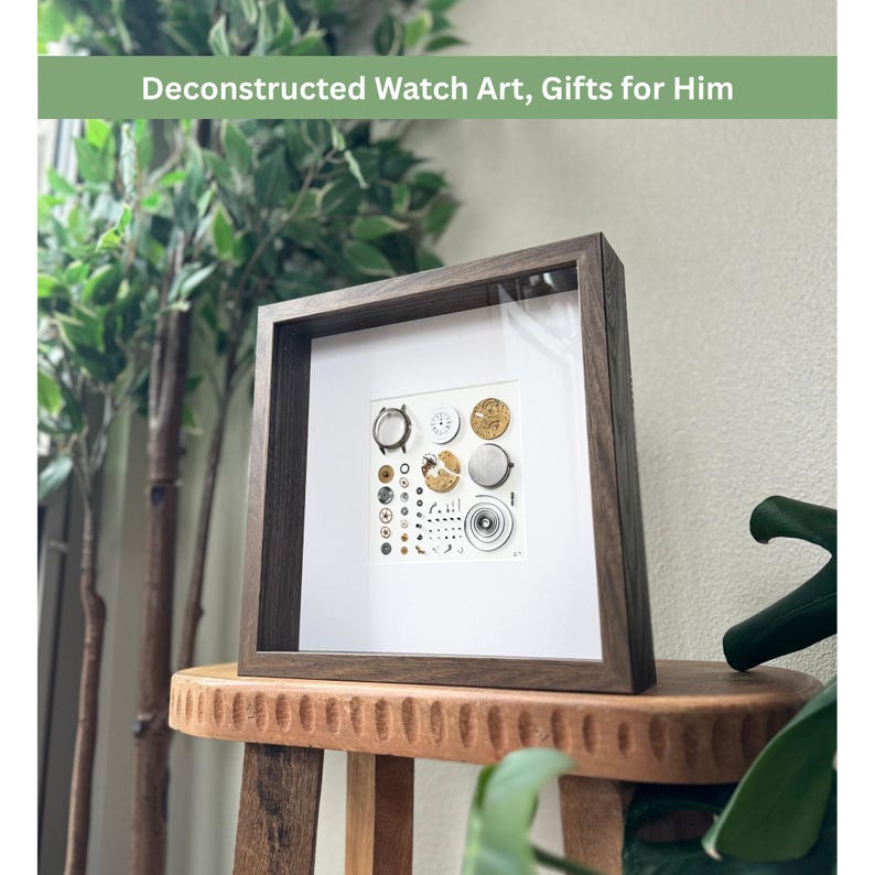 Puede incluir: Una obra de arte enmarcada que presenta piezas de reloj desmontadas. La obra de arte est&aacute; en un marco de madera marr&oacute;n oscuro con un passe-partout blanco. Los componentes del reloj est&aacute;n dispuestos sobre un fondo blanco. El texto en la parte superior dice "Deconstructed Watch Art, Gifts for Him."