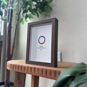 May include: A framed print featuring a watch bezel design with red, white, and blue accents. The print is set in a dark brown wooden frame with a white mat. The text "Rolex GMT Master II Pepsi" is visible.