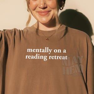 Puede incluir: Una camiseta marrón de manga corta con el texto blanco "mentally on a reading retreat" impreso en el pecho. La camiseta tiene cuello redondo y un corte holgado. La palabra "Espresso" está impresa en la esquina inferior izquierda.