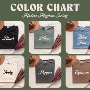 Puede incluir: Una carta de colores para Modern Mayhem Society con seis camisetas en negro, musgo, azul jean, marfil, pimienta y espresso. Cada camiseta se muestra con un sombrero marr&oacute;n y un manojo de hierba seca, con el nombre del color en letra cursiva blanca.