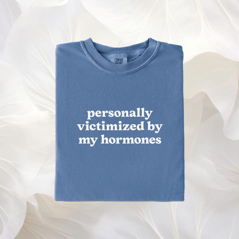Puede incluir: Una camiseta azul de cuello redondo con el texto blanco personally victimized by my hormones impreso en la parte delantera. La prenda tiene un cuello acanalado y una etiqueta en el escote. La tela tiene un acabado mate y s&oacute;lido en azul.