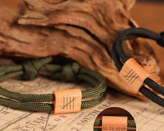 May include: Two bracelets with wooden accents. One bracelet is olive green with a wooden rectangular accent engraved with vertical lines. The other bracelet is black with a wooden rectangular accent engraved with vertical lines.
