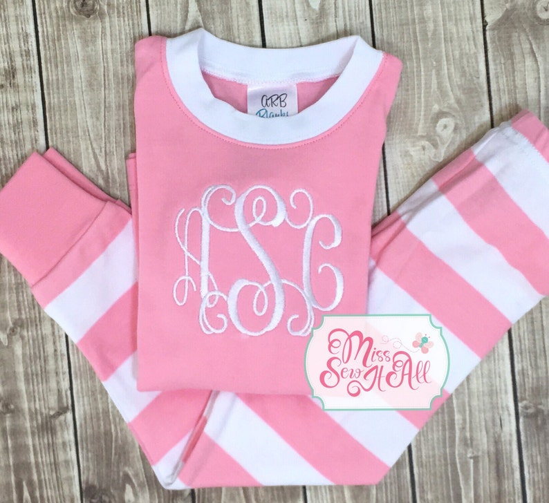 Puede incluir: Pijama a rayas rosa y blanco con un monograma blanco en la parte delantera. El pijama tiene un cuello y pu&ntilde;os acanalados blancos. El texto "Miss Sew It All" es visible en la esquina inferior derecha de la imagen.