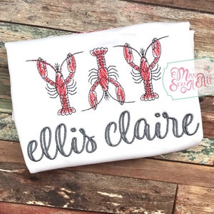 May include: White t-shirt with three red embroidered lobsters and the text "ellis claire" in gray cursive.