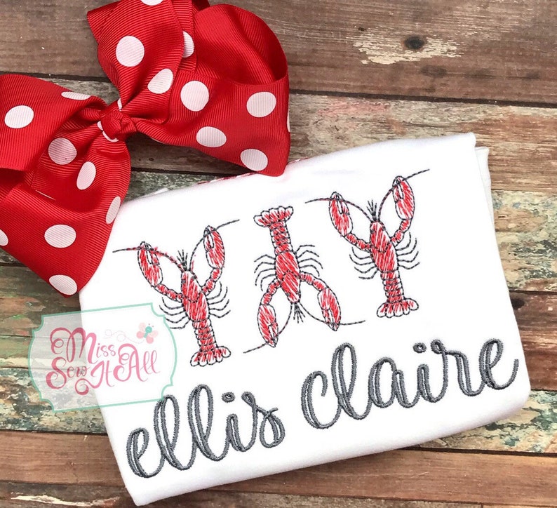 May include: White t-shirt with three embroidered red lobsters and the text "ellis claire" in gray cursive lettering.