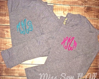 May include: Two gray long-sleeved shirts with embroidered monograms. The monogram on the left shirt is in turquoise blue and the monogram on the right shirt is in pink.