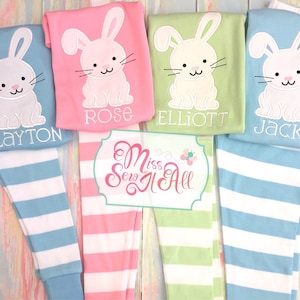 May include: Four pairs of striped pajamas with embroidered bunny rabbits and names. The pajamas are in pink, green, and blue with white stripes. The names are Clayton, Rose, Elliott, and Jack.
