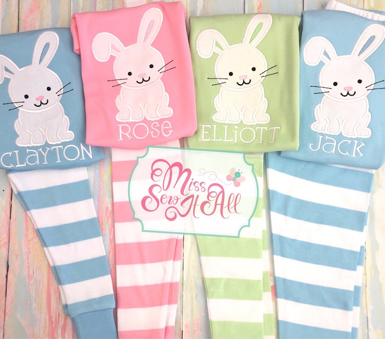 May include: Four pairs of striped pajamas with embroidered bunny rabbits and names. The pajamas are in pink, green, and blue with white stripes. The names are Clayton, Rose, Elliott, and Jack.