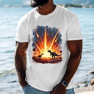 Op de afbeelding: Wit T-shirt met een afbeelding van twee dinosaurus silhouetten tegen een vurige meteorietenregen. Het ontwerp bevat palmbomen en de tekst "Echo from the Stone".