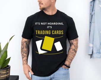 May include: A black t-shirt with the text "It's not hoarding, it's trading cards" in white and a graphic of yellow and white playing cards.