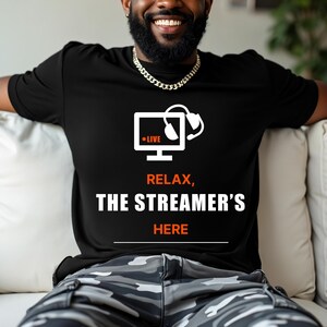 May include: A black t-shirt with a white graphic of a computer monitor with a headset and the words "LIVE", "RELAX", "THE STREAMER'S", and "HERE".