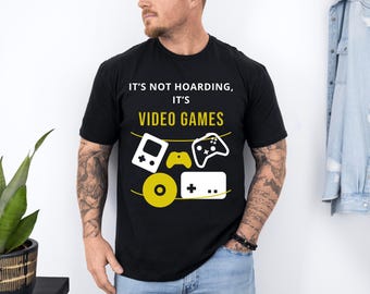 May include: Black t-shirt with white text that reads "It's not hoarding, it's video games". The shirt features a graphic of a video game controller, a game cartridge, and a video game disc.