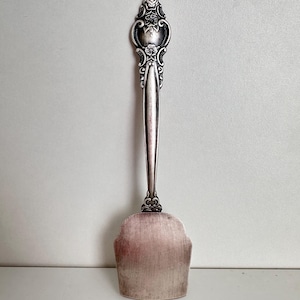 May include: A silver serving utensil with an ornate handle and a wide, flat blade. The handle is decorated with floral designs.