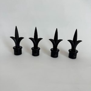 May include: Four matte black curtain rod finials, each featuring a pointed spearhead design with curved side accents and a cylindrical base with a small visible screw on the side for secure attachment to a rod.