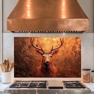 Op de afbeelding: Een koperen afzuigkap voor de keuken met een achterwand met een close-up van een hert met gewei in een bosrijke omgeving.