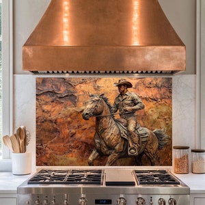 May include: A copper range hood above a stainless steel stove. A backsplash features a bronze-colored relief sculpture of a cowboy on horseback. The sculpture is set against a textured, reddish-brown background. The kitchen has white countertops and windows.