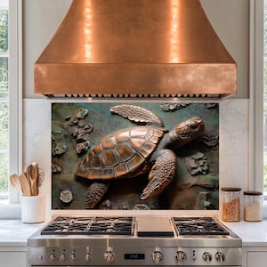 May include: A copper kitchen range hood with a decorative backsplash featuring a bronze-colored sea turtle sculpture. The turtle is surrounded by textured, brown and green accents.