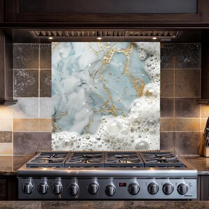 May include: A kitchen backsplash with a marble and gold design. The marble is light blue and white with gold veins. The design is topped with a layer of white foam with bubbles.