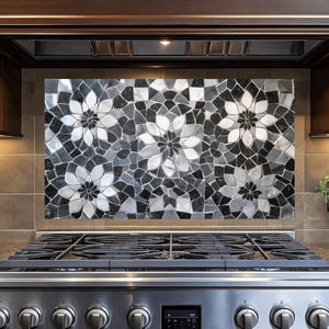 Pode incluir: Um fogão de aço inoxidável com um protetor de respingos de mosaico preto e branco com um padrão floral. O protetor de respingos é feito de azulejos pequenos de formas irregulares.