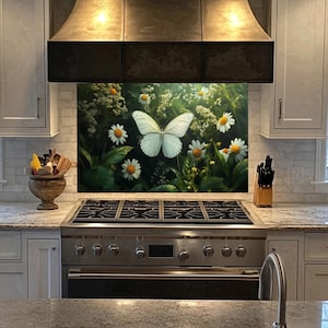 May include: A white butterfly with black markings is perched on a green leafy background with white daisies. The butterfly is in the center of the image and is surrounded by flowers. The image is a kitchen backsplash.