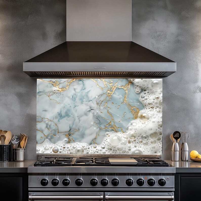 May include: A kitchen backsplash with a marble and gold design. The backsplash is behind a stainless steel stove with a range hood above it.