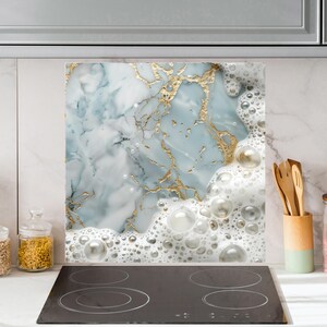 May include: A kitchen backsplash with a marble and gold design. The marble is light blue and white with gold veins. The design is topped with a layer of white foam with large bubbles.