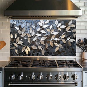 Può includere: Un piano cottura in acciaio inox con cinque bruciatori e un paraschizzi in mosaico nero con un motivo a foglie d'argento.