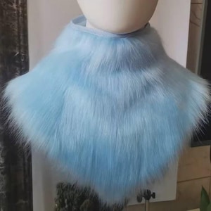 May include: A light blue faux fur collar. The collar is fluffy and soft, with a high neckline. The fur is a solid, light blue colour. The collar is designed to be worn around the neck.