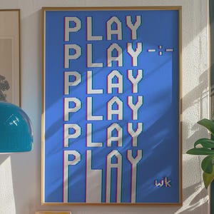 May include: A framed art print with the word "PLAY" repeated vertically in a pixelated font against a blue background. The print has a gold frame and is displayed in a room with a retro aesthetic, including a record player and orange storage unit.