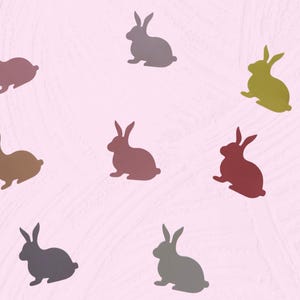 May include: A pattern of eight bunny silhouettes in various colors, including shades of pink, brown, gray, and green, against a light pink background. The bunnies are in a sitting position, with their ears upright.